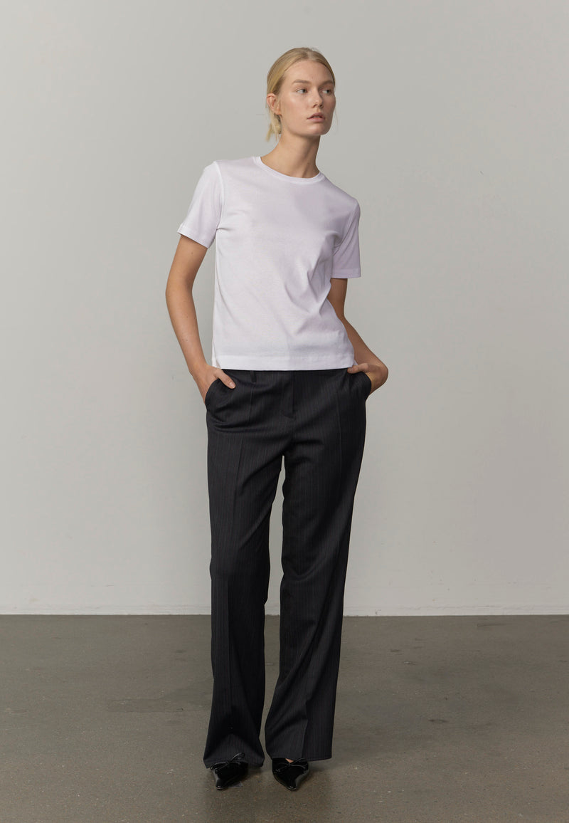 A woman modeling a white short-sleeve crewneck t-shirt and dark charcoal gray wide-leg trousers, from Herskind.