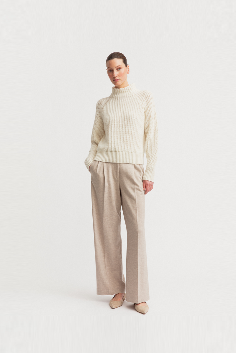 A woman modeling a cream Iris Von Arnim ribbed mock-neck sweater.