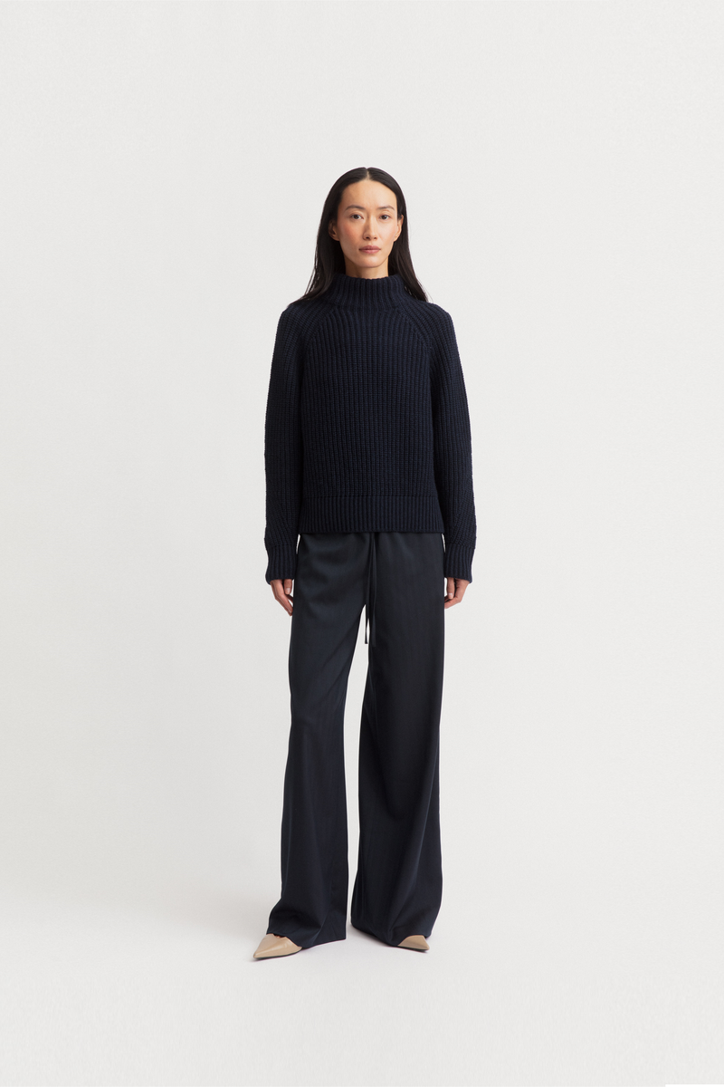 Model wearing a dark navy ribbed mock-neck sweater and matching dark wide-leg trousers from Iris Von Arnim.