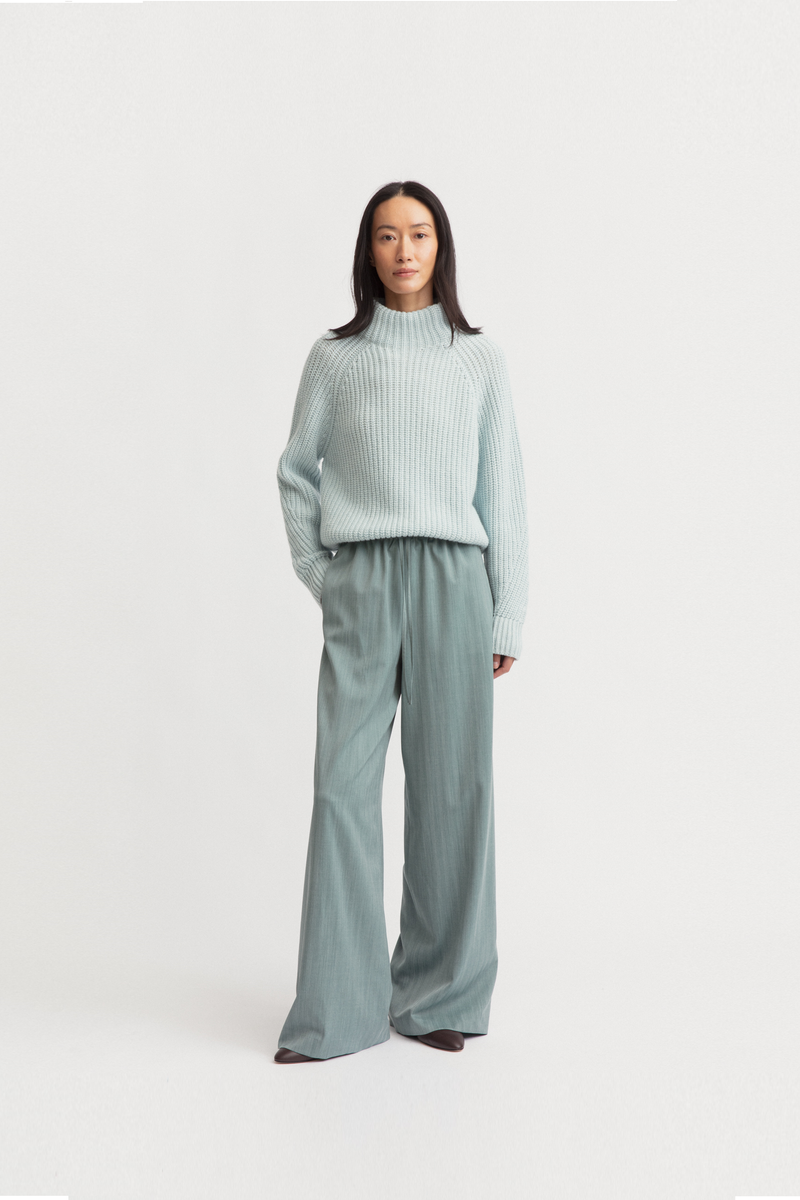 Model wearing a light sage green ribbed turtleneck sweater and matching wide-leg trousers from Iris Von Armin. 