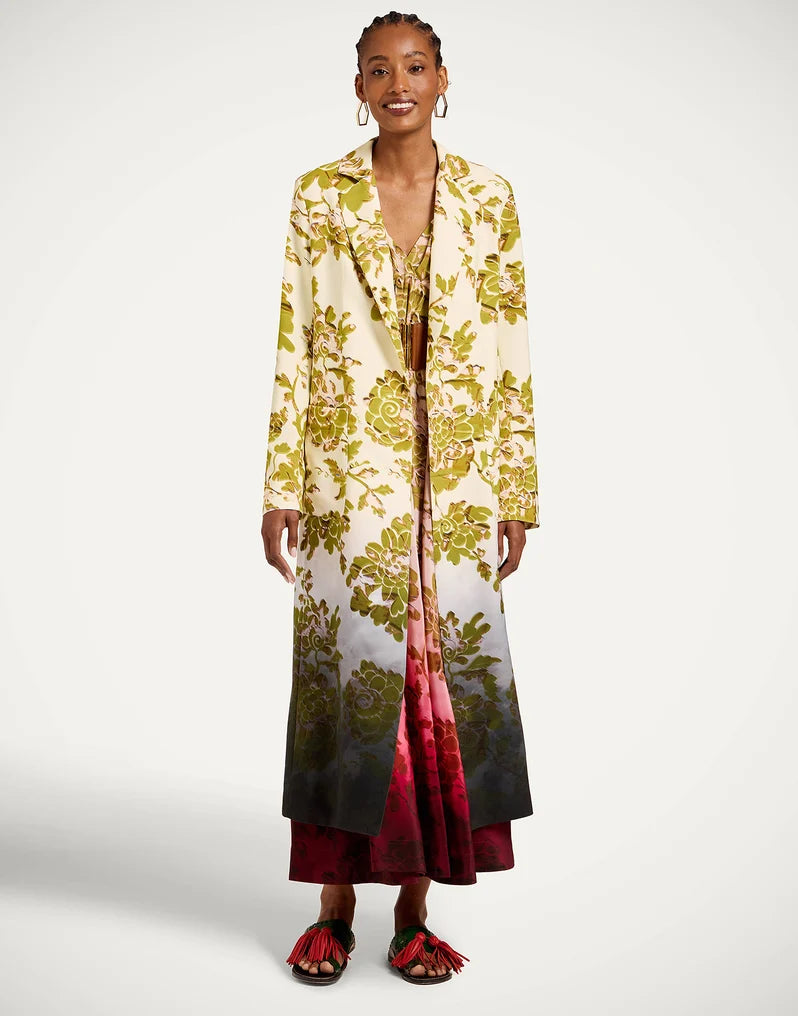 A model wearing a long cream-colored open-front coat with a green and yellow floral print, a red and pink floral inner dress, and red tassel slide sandals from La Double J. 
