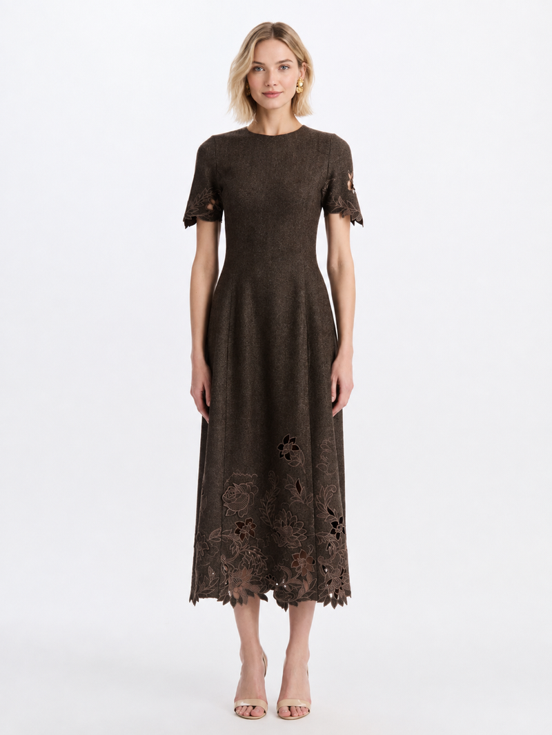 A model in a dark brown midi dress with short sleeves, featuring a fitted bodice, flared skirt, and intricate floral lace cutouts along the hem and sleeve cuffs, by Oscar de la Renta. 