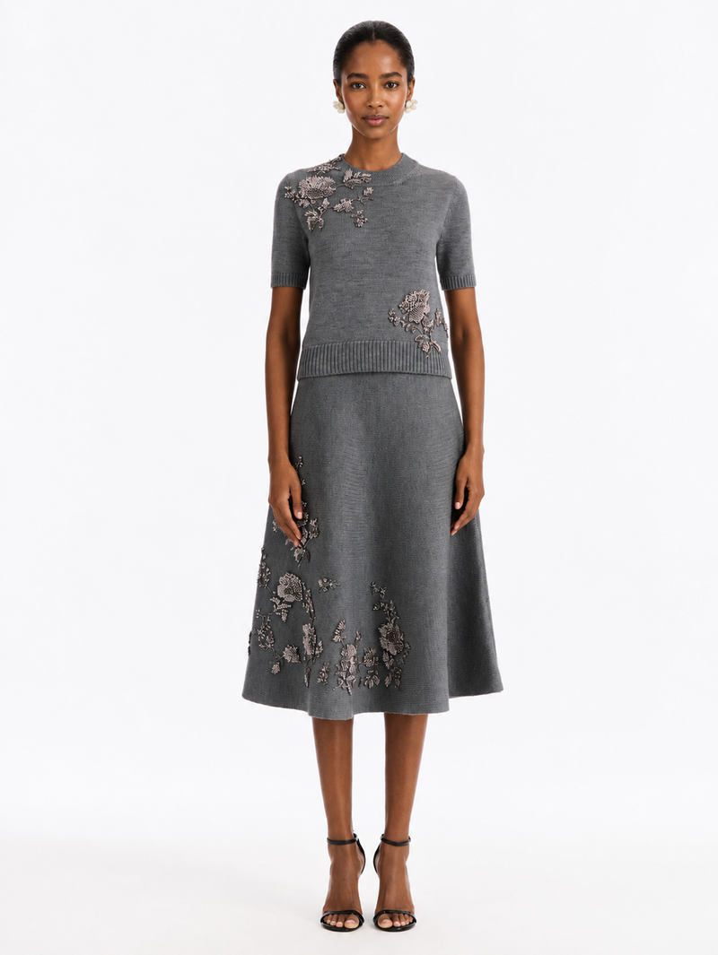 A model wearing a gray short-sleeve knit top and matching A-line midi skirt set, both decorated with floral embroidery from Oscar de la Renta.