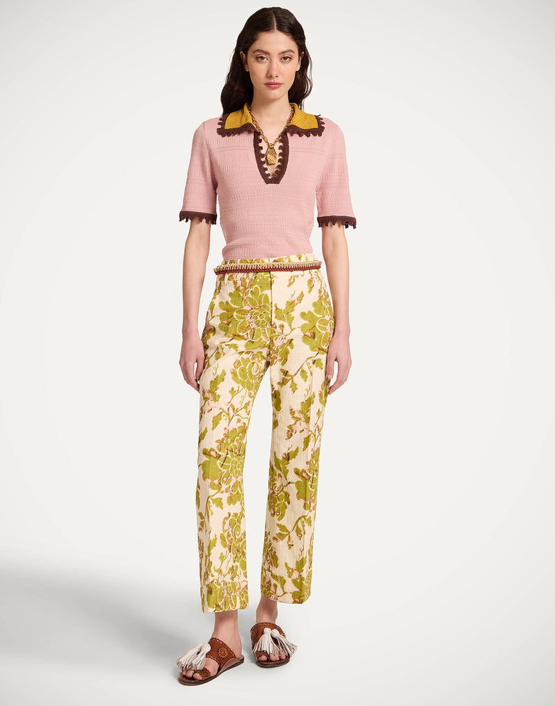 A model  wearing a pink short-sleeve knit top with a yellow and brown collar and trim, paired with cream trousers featuring a yellow-green botanical pattern, and brown sandals from La Double J.