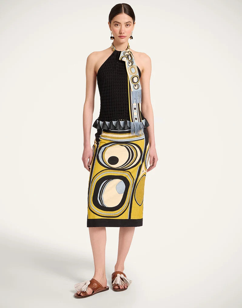 A model stands wearing a sleeveless halter dress with a black ribbed top and a yellow, black, white, and blue abstract graphic skirt, paired with brown sandals from La Double J. 