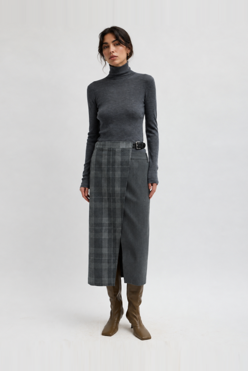 A model wearing a dark gray ribbed turtleneck sweater, a matching gray plaid wrap skirt with a black belt by Tibi. 