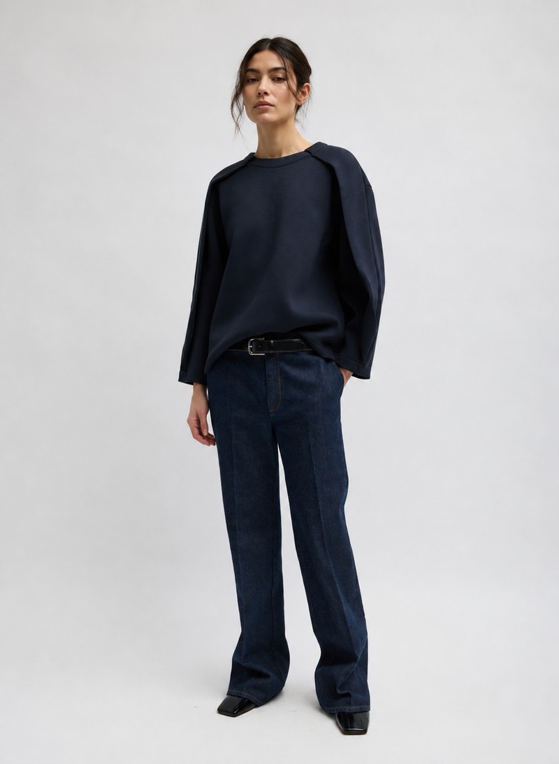 A mode wearing a dark navy long-sleeve top with draped shoulders and matching dark navy wide-leg trousers by Tibi. 
