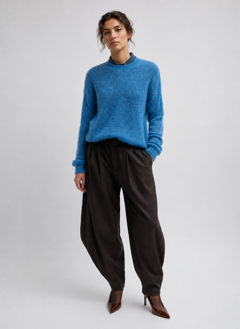 A model wearing a bright blue knit crewneck sweater, dark brown wide-leg trousers, and brown pointed-toe heels from Tibi. 