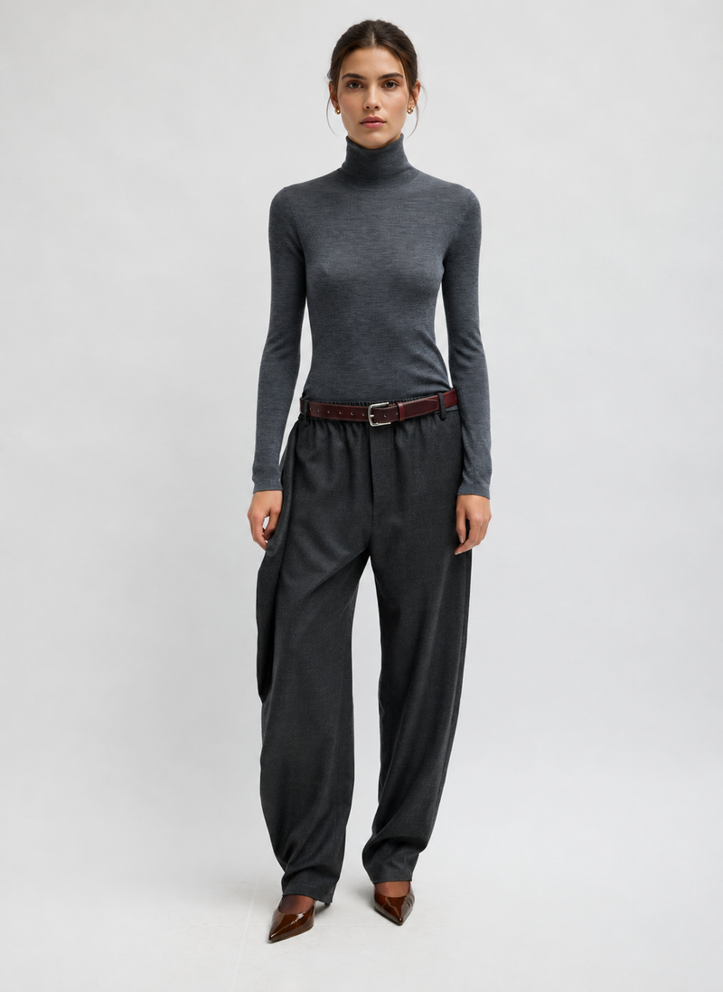 A mode wearing a dark gray ribbed turtleneck sweater, dark charcoal wide-leg trousers, a dark red belt, and brown pointed-toe heels by Tibi. 