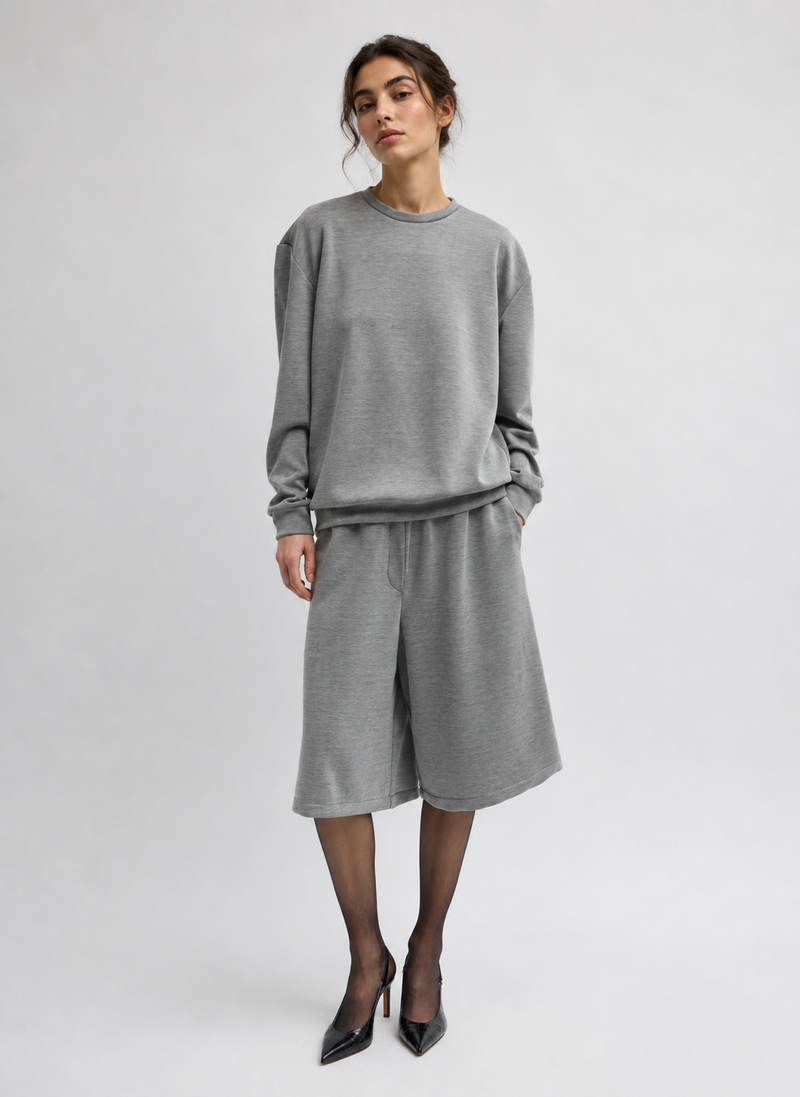 A model a matching gray knit lounge set consisting of a long-sleeve crewneck sweatshirt and high-waisted shorts, paired with black pointed-toe heels by Tibi. 