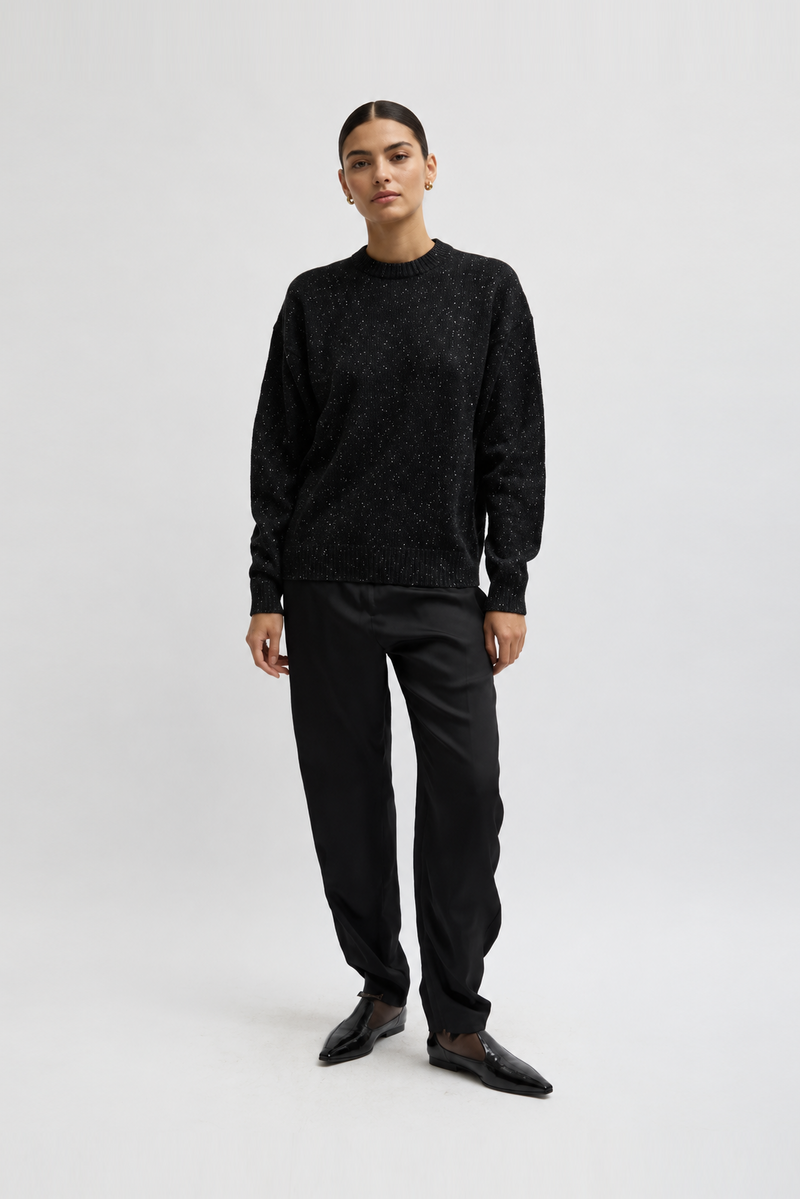 A mode wearing a black textured knit crewneck sweater, black trousers, and black leather shoes by Tibi.