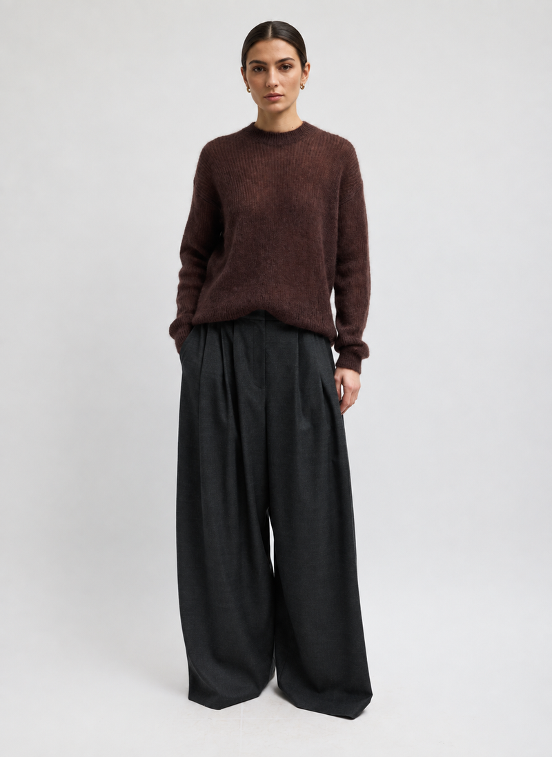 A model wearing a fuzzy dark brown crewneck sweater and wide-leg black trousers by Tibi. 
