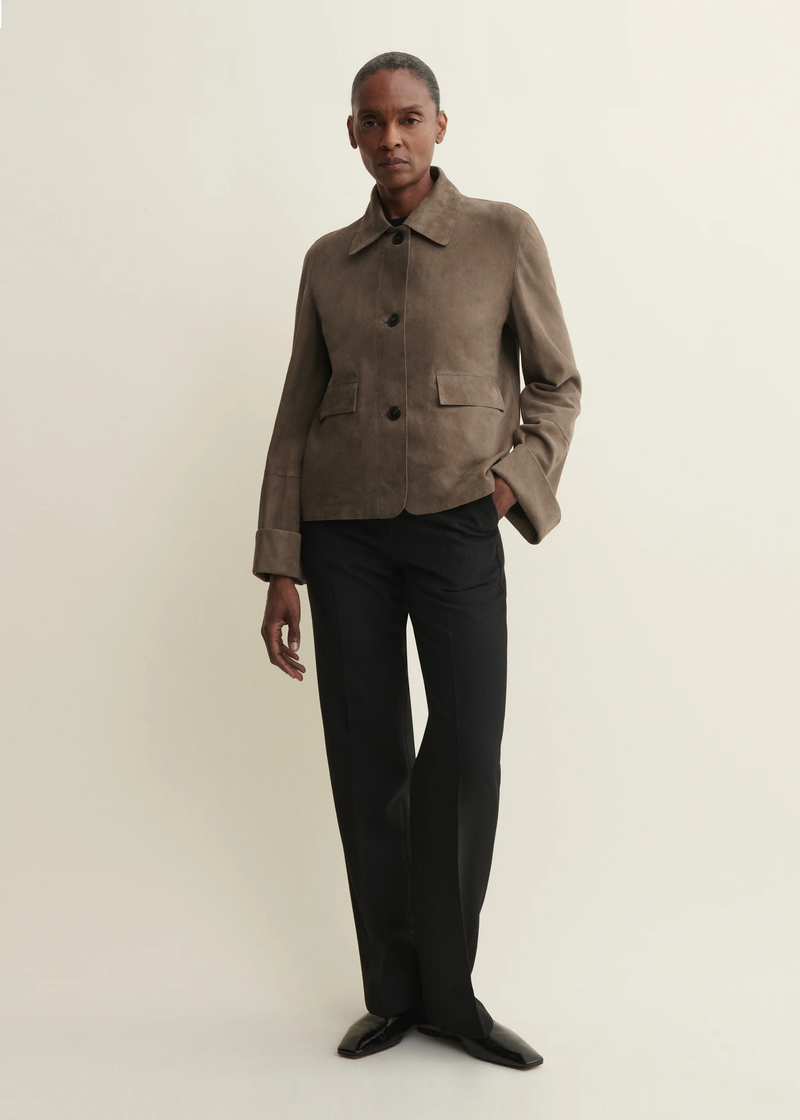 A model wearing a taupe-brown suede jacket with black trousers and black shoes from Arma. 
